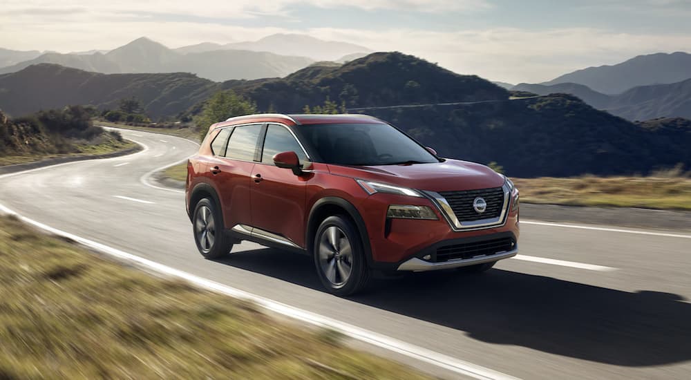 A red 2023 Nissan Rogue is shown from the side driving on an open road.