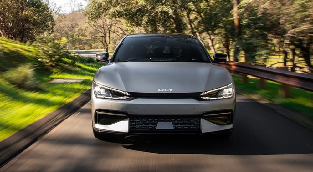 A silver 2023 Kia EV6 is shown from the front speeding down a tree-lined road.