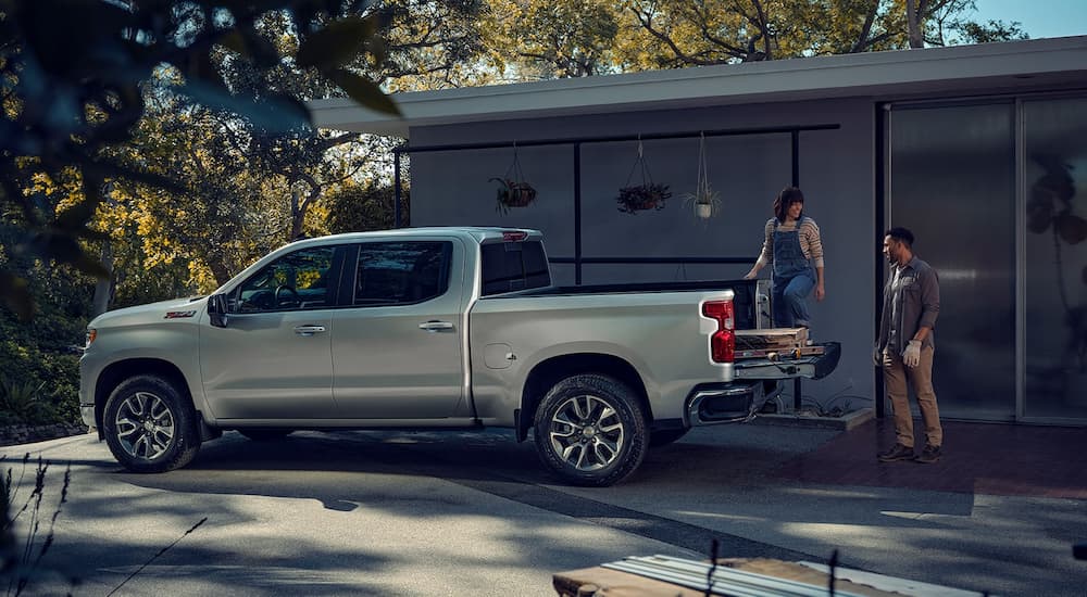 A couple is shown loading the bed of a silver 2023 Chevy Silverado 1500 Z71 in a driveway.