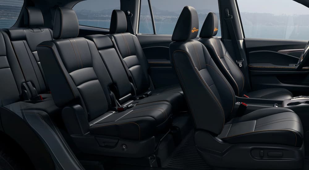 The black interior of a 2023 Honda Pilot TrailSport shows rows of seating near a Honda dealer.