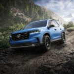 A blue 2023 Honda Pilot Trailsport is shown driving on a muddy trail.