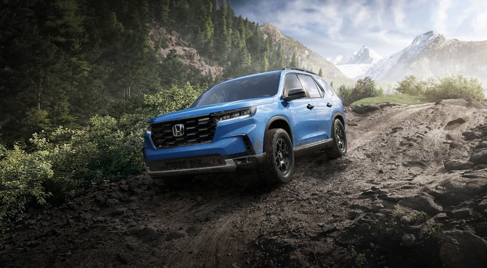 A blue 2023 Honda Pilot Trailsport is shown driving on a muddy trail.