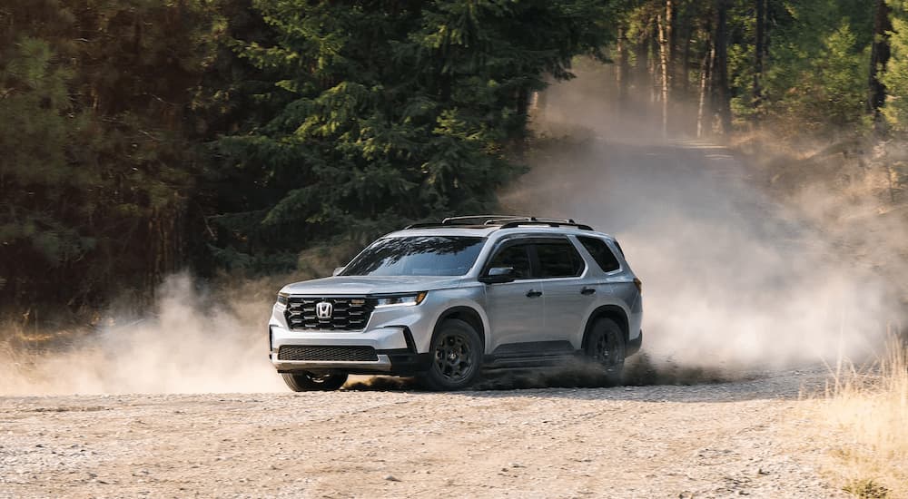 A silver 2023 Honda Pilot TrailSport is shown off-roading on a dusty trail.