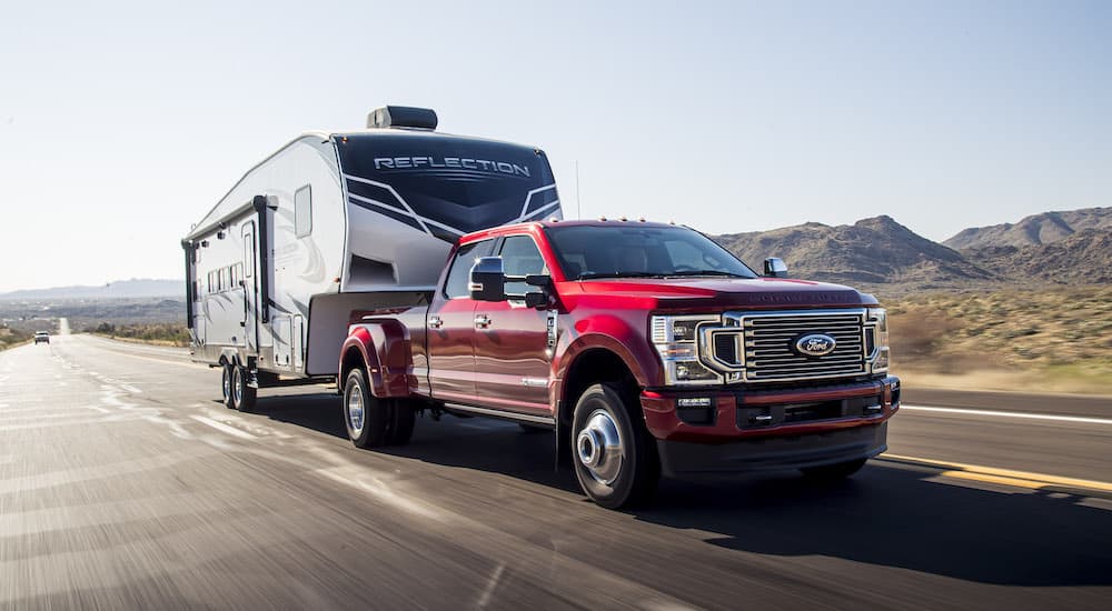 A red 2023 Ford F-350 Super Duty is shown from the front at an angle while towing a large camper..