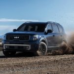 A blue 2023 Kia Telluride is shown off-roading on a dirt path.