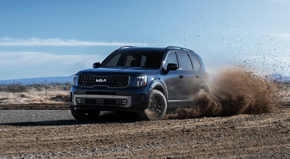 A blue 2023 Kia Telluride is shown off-roading on a dirt path.