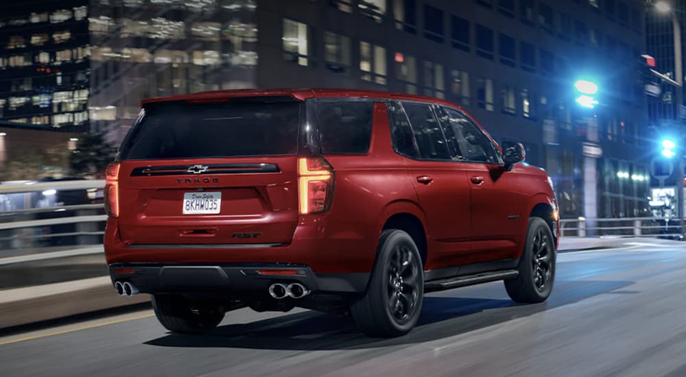 A red 2023 Chevy Tahoe is shown from the rear driving through a city at night.