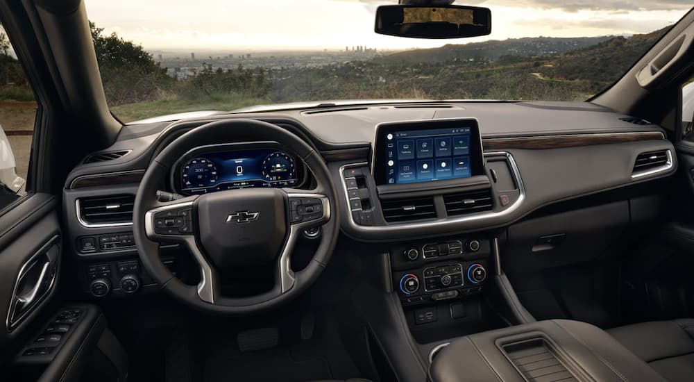 The black interior of a 2023 Chevy Tahoe shows the steering wheel and infotainment screen.