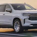 A white 2023 Chevy Tahoe is shown from the front driving on an open road.