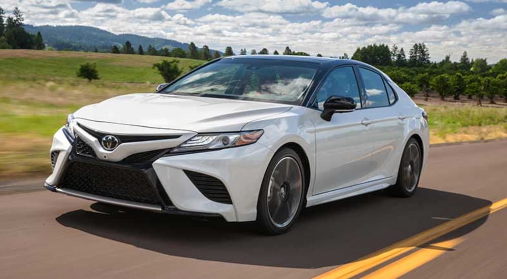 A white 2018 Toyota Camry for sale is shown driving on an open road.