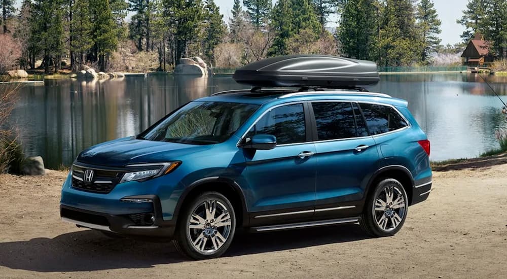 A blue 2020 Honda Pilot is shown parked on sand next to a lake.