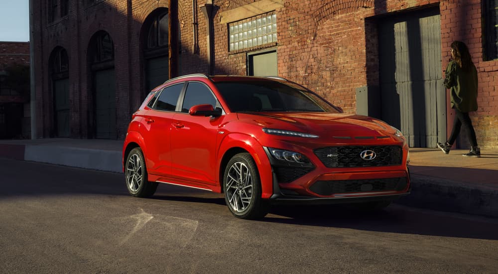 A red 2021 used Hyundai Kona for sale is shown parked on the side of a city street.