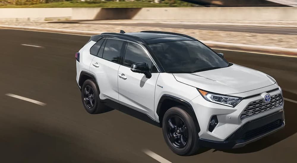 A white 2020 Toyota RAV4 Hybrid is shown driving on an empty highway.