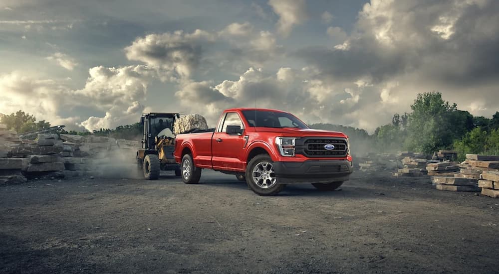 Heavy machinery is shown putting rocks in the bed of a red 2022 Ford F-150 XL at a construction site.