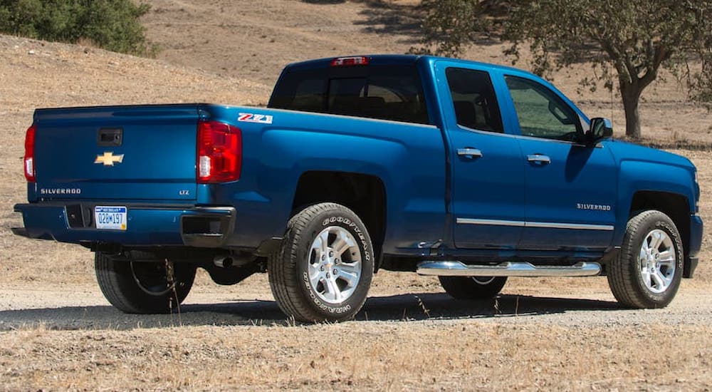 A blue 2018 Chevy Silverado 1500 is shown from the rear at an angle after leaving a dealer that has used trucks for sale.
