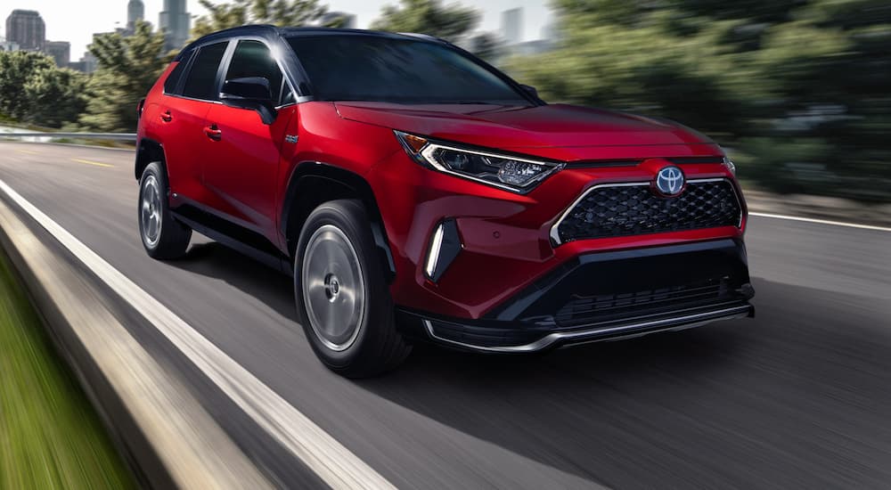 A red 2021 Toyota RAV4 Prime is shown driving on a city highway.