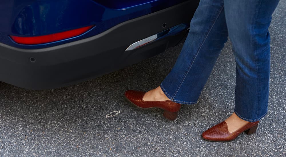 A person is shown opening the trunk of a dark blue 2023 Chevy Equinox.