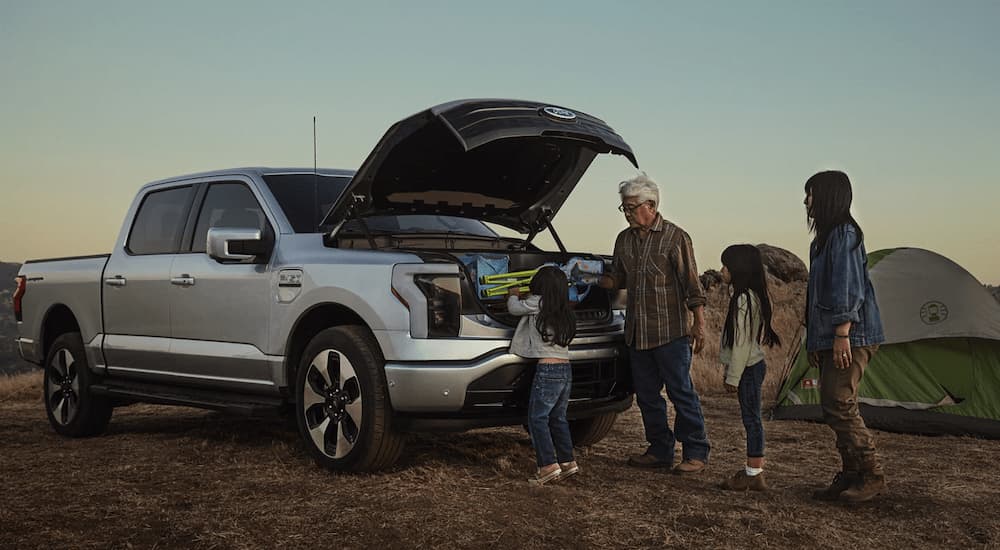A family is shown getting camping gear out of the frunk of a silver 2023 Ford F-150 Lightning.