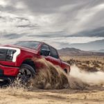 A red 2023 Ford F-150 Lightning is shown driving in a sandy desert.