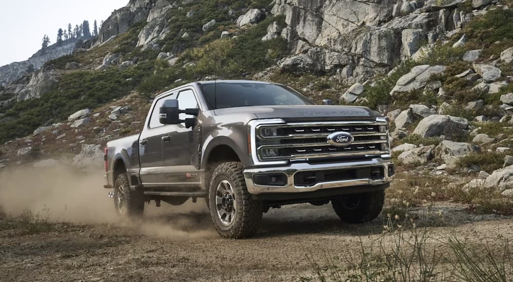 A grey 2023 Ford F-350 is shown from the front driving on a dirt road.