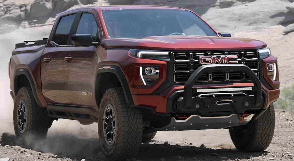 A red 2023 GMC Canyon AT4X is shown from the front driving on a dirt road during a 2023 GMC Canyon vs 2023 Nissan Frontier comparison. 