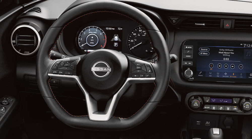 The black interior of a 2023 Nissan Kicks shows the steering wheel and infotainment screen.