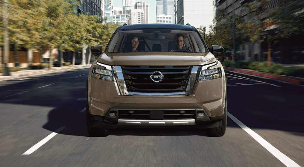 A tan 2023 Nissan Pathfinder is shown from the front driving on an open road.