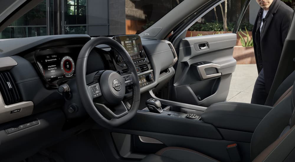 The grey interior of a 2023 Nissan Pathfinder shows the steering wheel and infotainment screen.