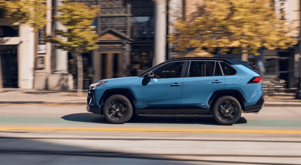 A blue 2023 Toyota RAV4 Hybrid XSE is shown from the side driving on a city street.