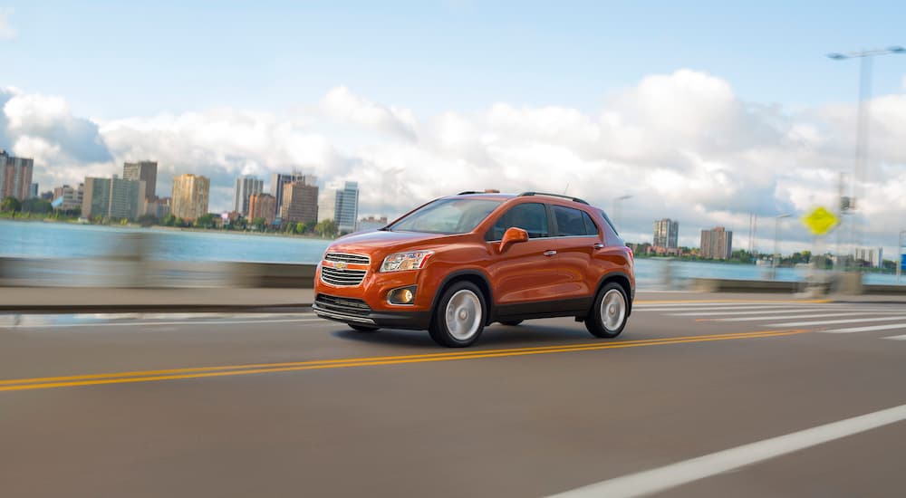 An orange 2015 Chevy Trax is shown driving past a city.