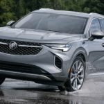 A silver 2023 Buick Envision is shown driving through a puddle.