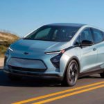 A light blue 2023 Chevy Bolt EV is shown driving on an open road after leaving a Chevy dealer.