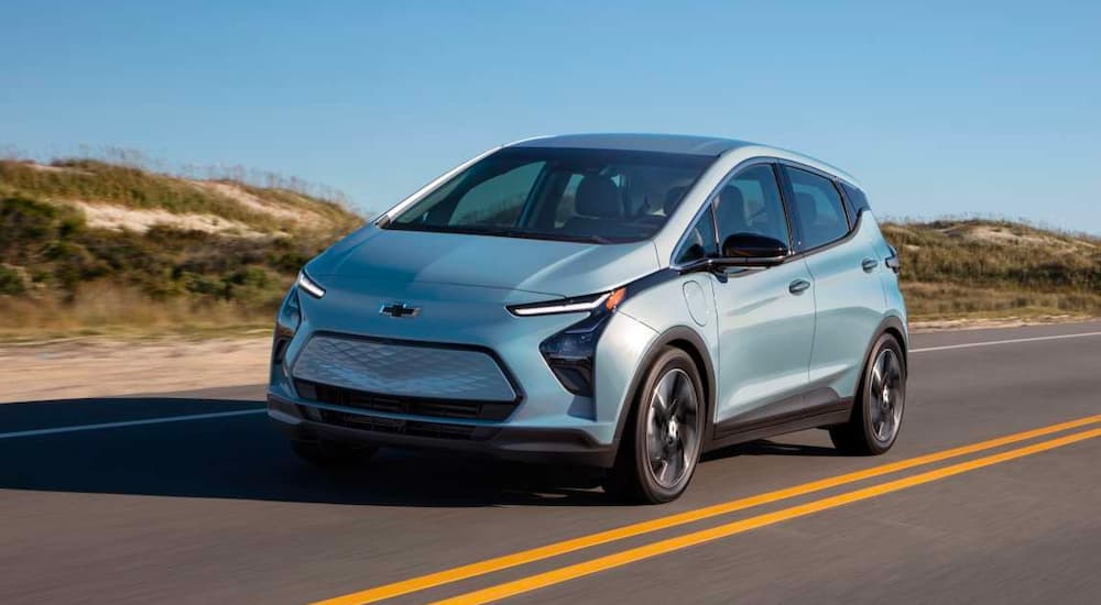 A light blue 2023 Chevy Bolt EV is shown driving on an open road after leaving a Chevy dealer.
