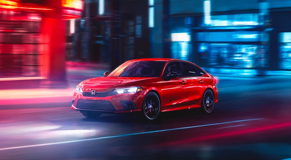 A red 2022 Honda Civic Sport is shown on a city street at night.