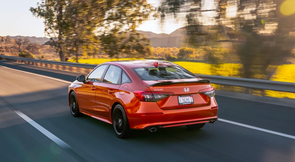 An orange 2023 Honda Civic Si is shown driving on an open road after leaving a Honda dealer near you.
