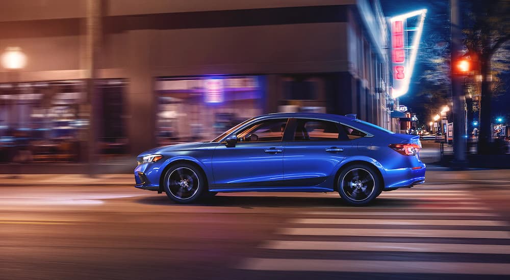A blue 2022 Honda Civic Sport is shown from the side driving on a city street at night.