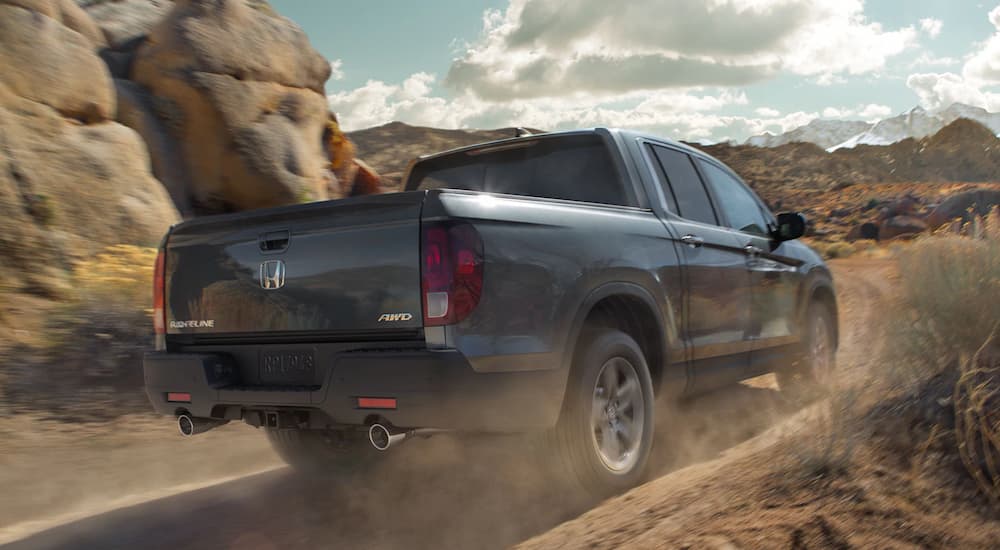 A grey 2022 Honda Ridgeline RTL-E is shown from a rear angle driving on a dusty trail.