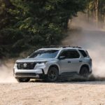 A grey 2023 Honda Pilot Trailsport is shown off-roading on a dusty trail.