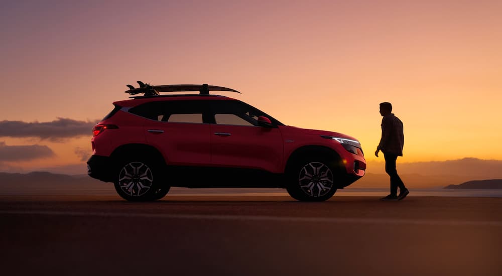 An orange 2022 Kia Seltos for sale is shown from the side at dusk.