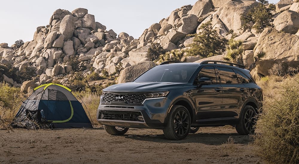 A grey 2023 Kia Sorento is shown parked at a remote mountainside campsite.