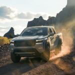 A grey 2023 Nissan Frontier Pro-4x is shown driving on a dusty rocky trail.