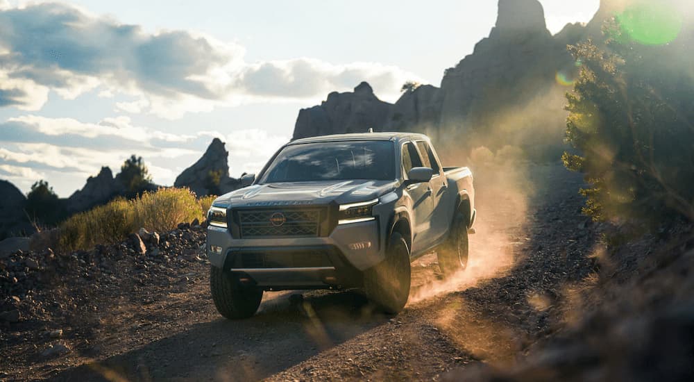 A grey 2023 Nissan Frontier Pro-4x is shown driving on a dusty rocky trail.