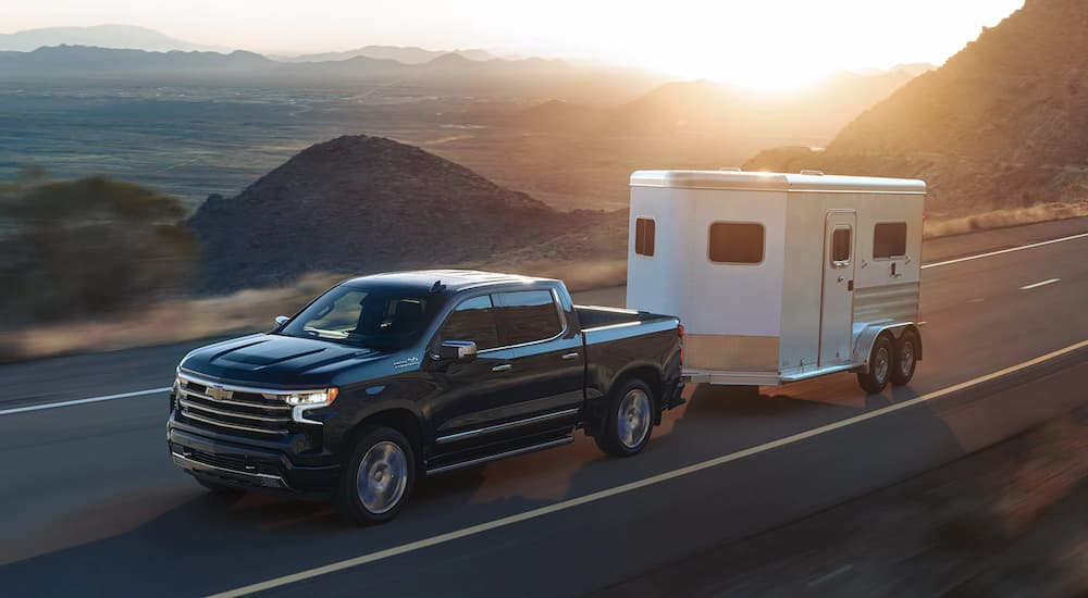 A black 2023 Chevy Silverado 1500 High Country is shown towing a white enclosed trailer.