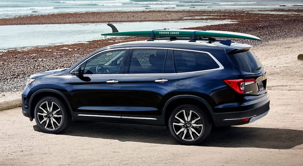 A dark blue 2019 Honda Pilot is shown at a beach with a surfboard on the roof.