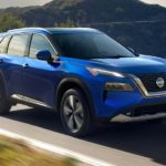 A blue 2021 Nissan Rogue for sale is shown driving on a winding road.
