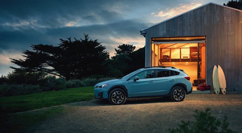 A light blue 2018 Subaru Crosstrek Limited is shown in front of a garage and surfboards.