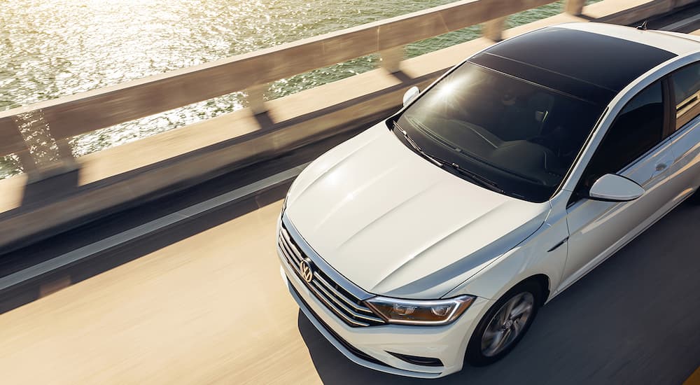 A popular VW for sale, a white 2022 Volkswagen Jetta, is shown driving on a bridge. 