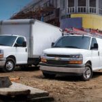 A white 2022 Chevy Express van and truck are shown parked at a construction site.