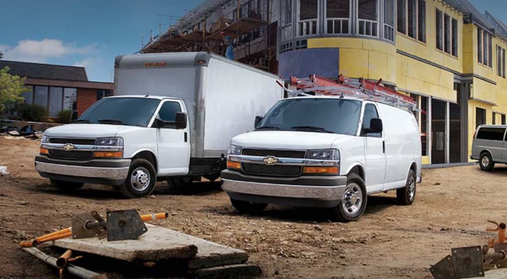 A white 2022 Chevy Express van and truck are shown parked at a construction site.