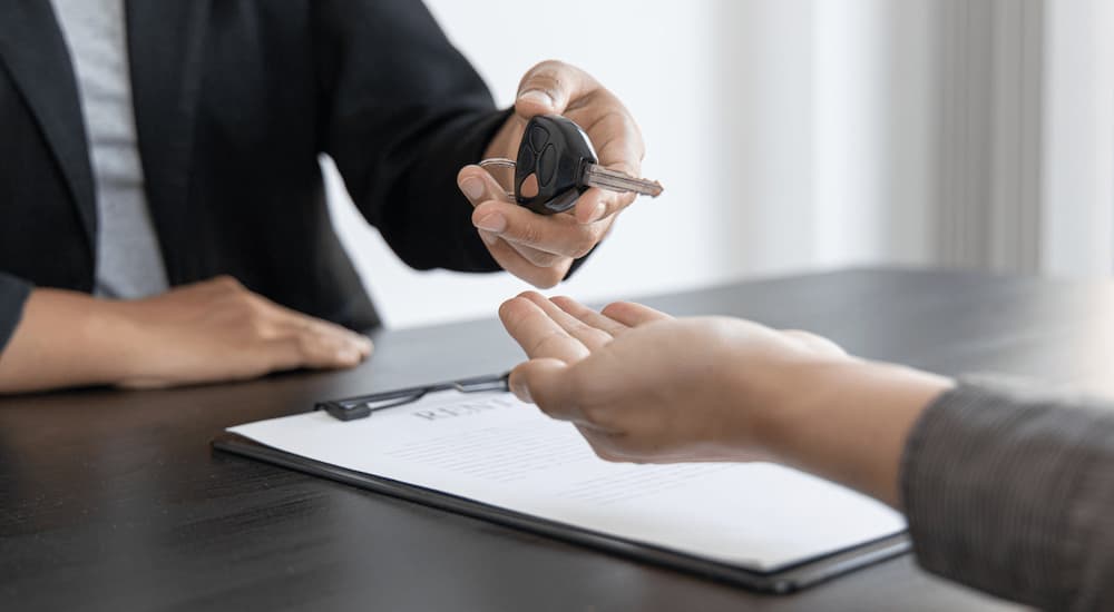 A car salesman is shown handing a car key to a customer.